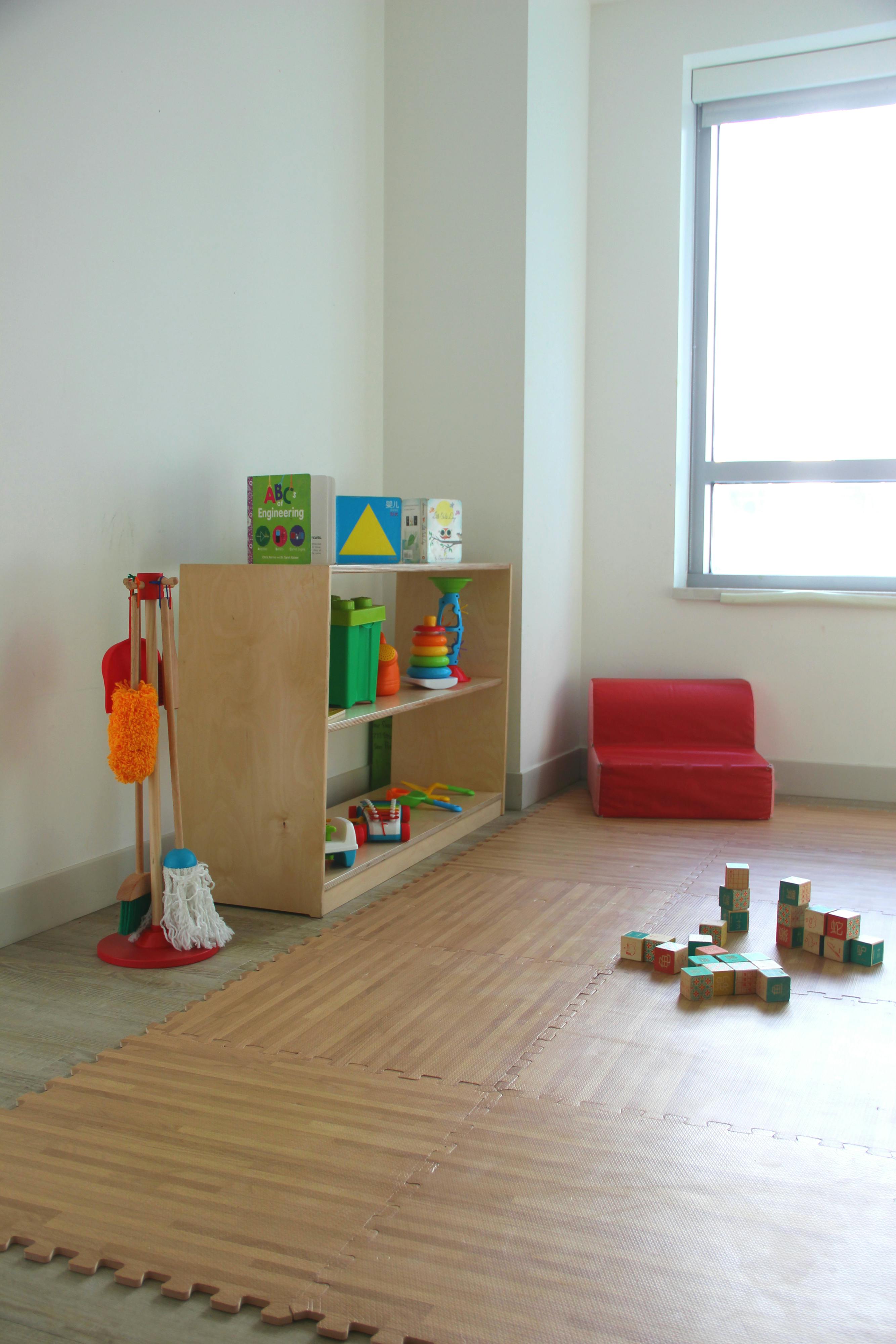Playroom with toy shelf, cleaning set, red child-sized couch, and wooden blocks