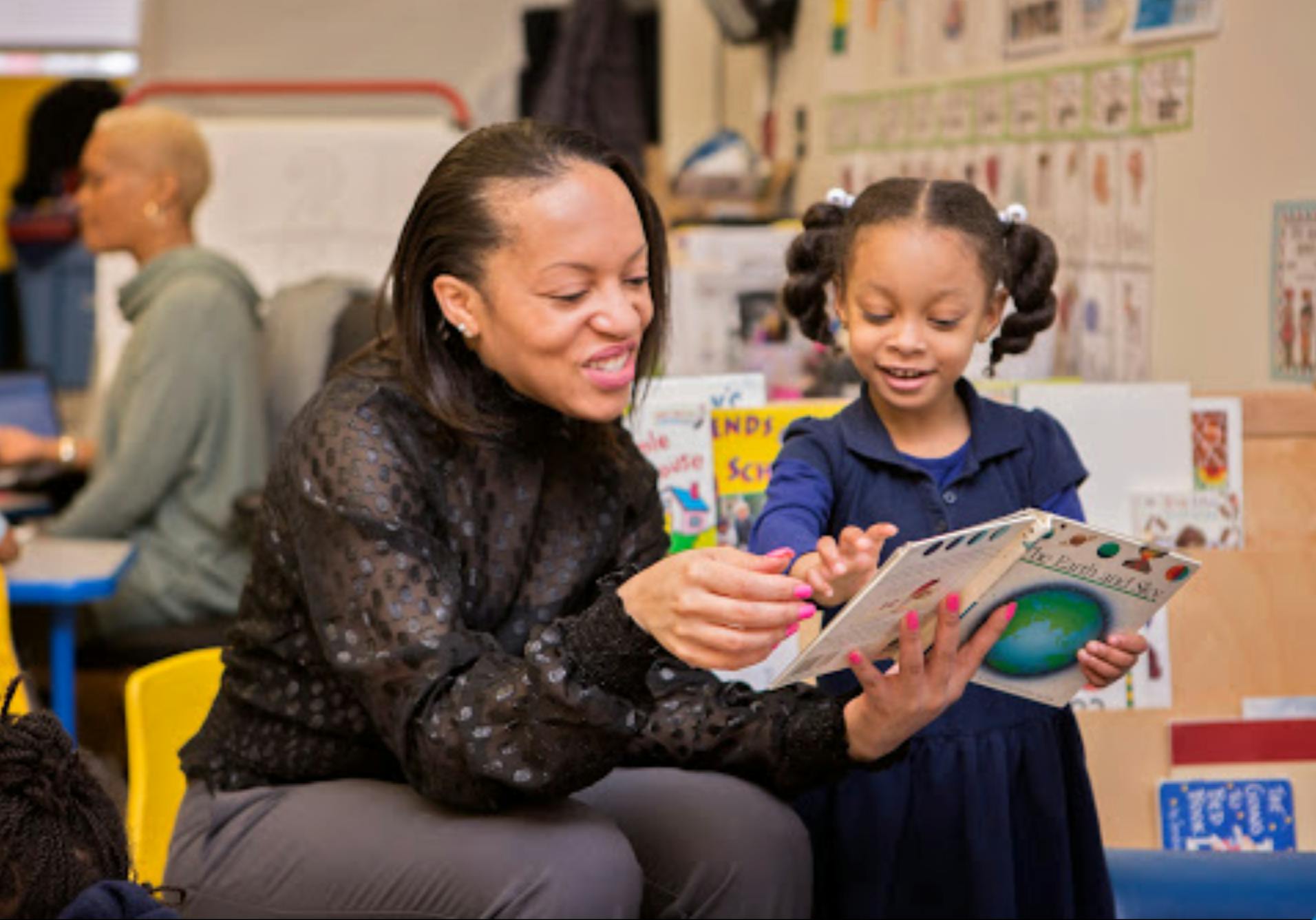Adult and child reading a book together in a classroom