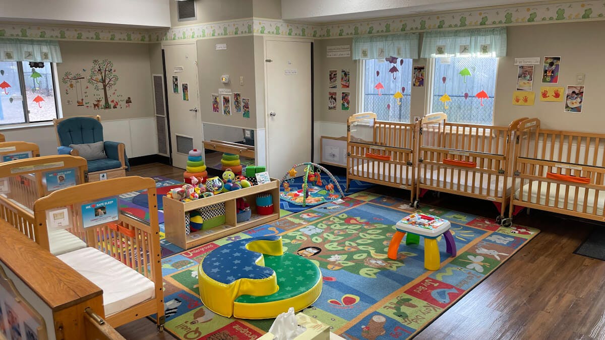 A colorful daycare classroom with cribs, playmats, and toys