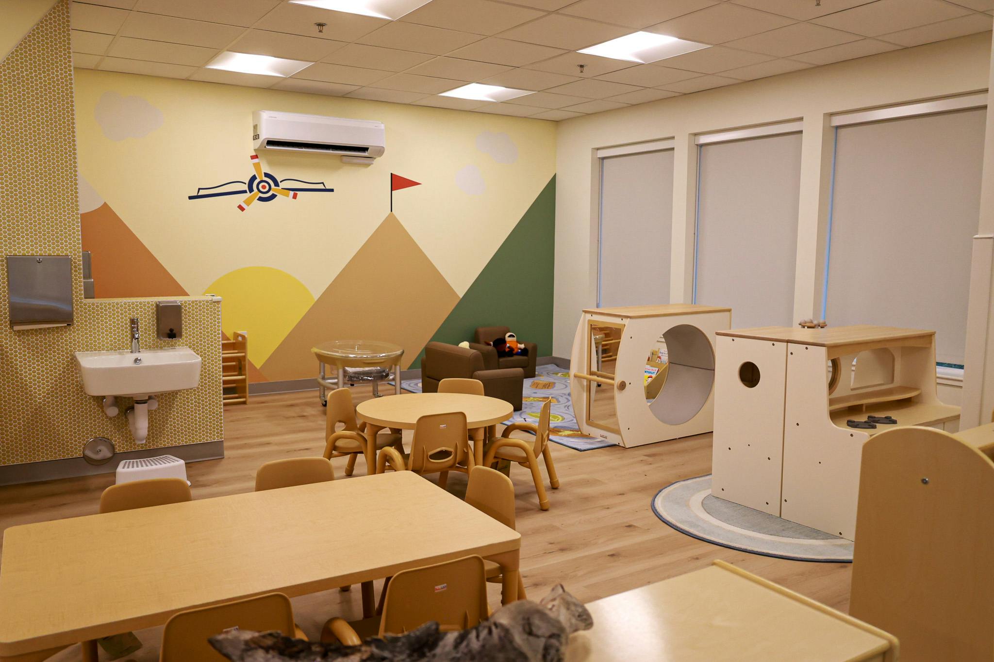 Childcare room with small tables, chairs, and play equipment