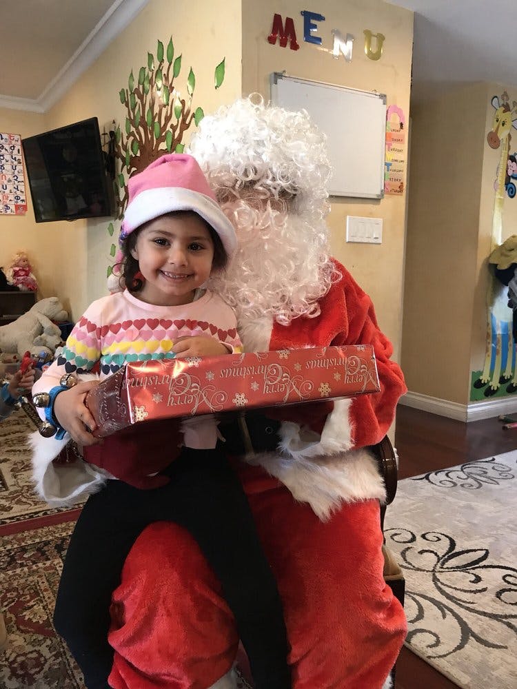Child in a pink hat sitting on a person dressed as Santa, holding a gift