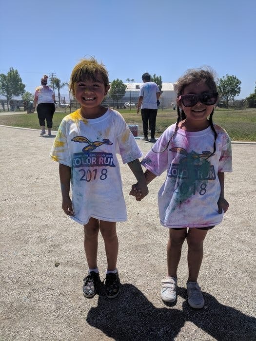 Two children holding hands, wearing white shirts with colorful powder