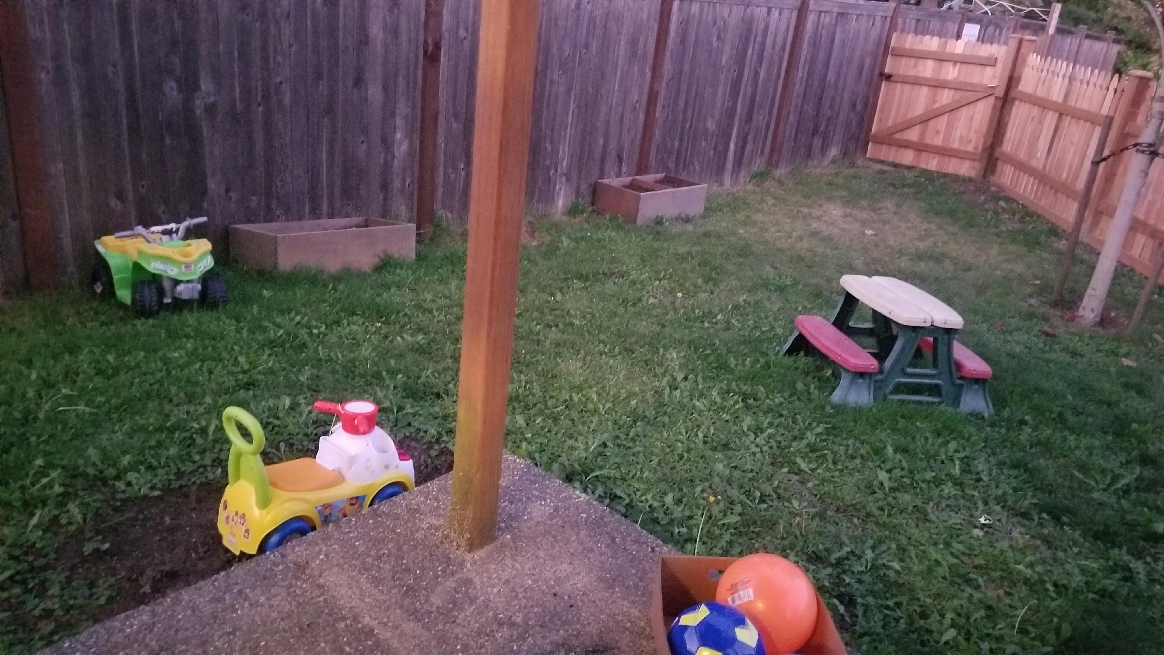Toy ride-on vehicles and a child's picnic table in a grassy yard