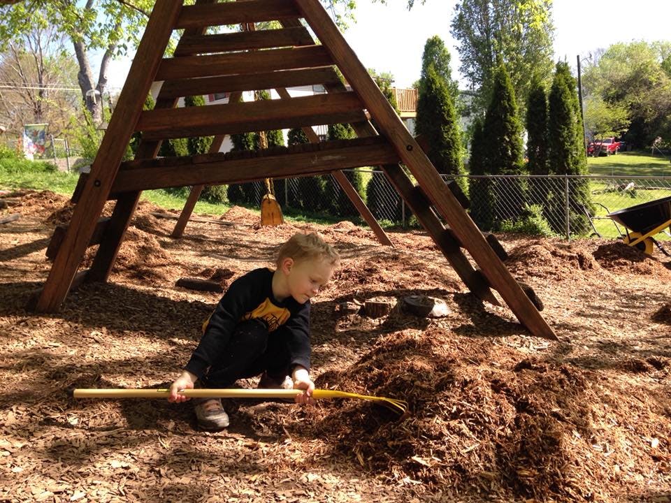 Child playing with a shovel in wood chips under a wooden play structure