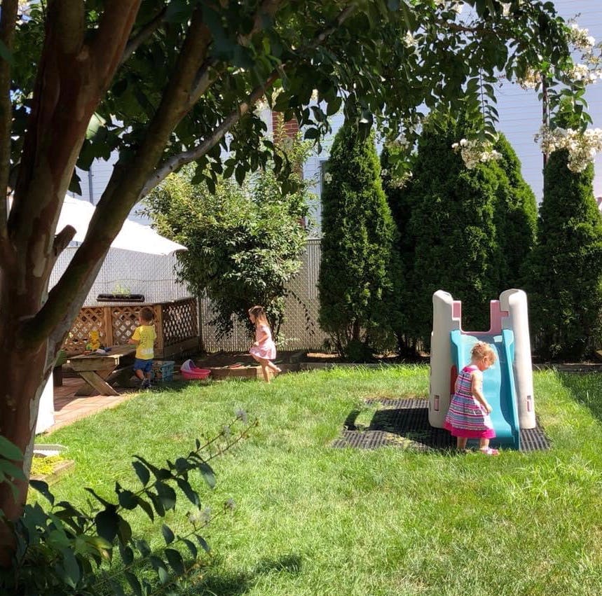 Children playing in a grassy backyard with a small slide