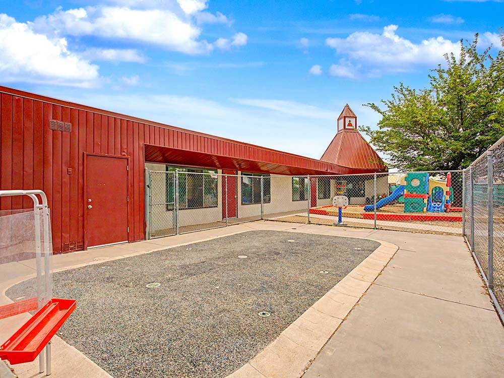 Red building and fenced playground with slide, sand, and splash pad area