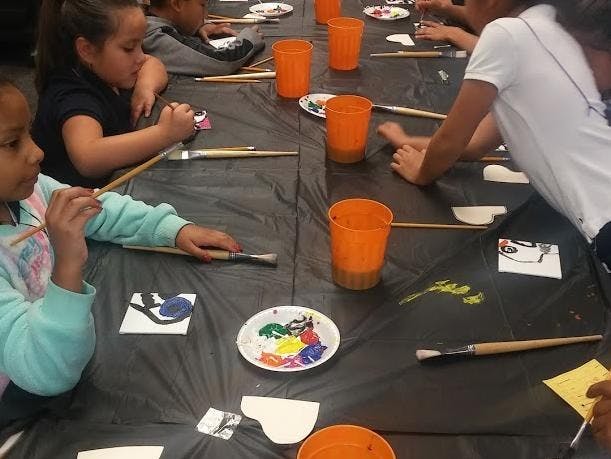 Children painting at a table with brushes, paint, and orange cups