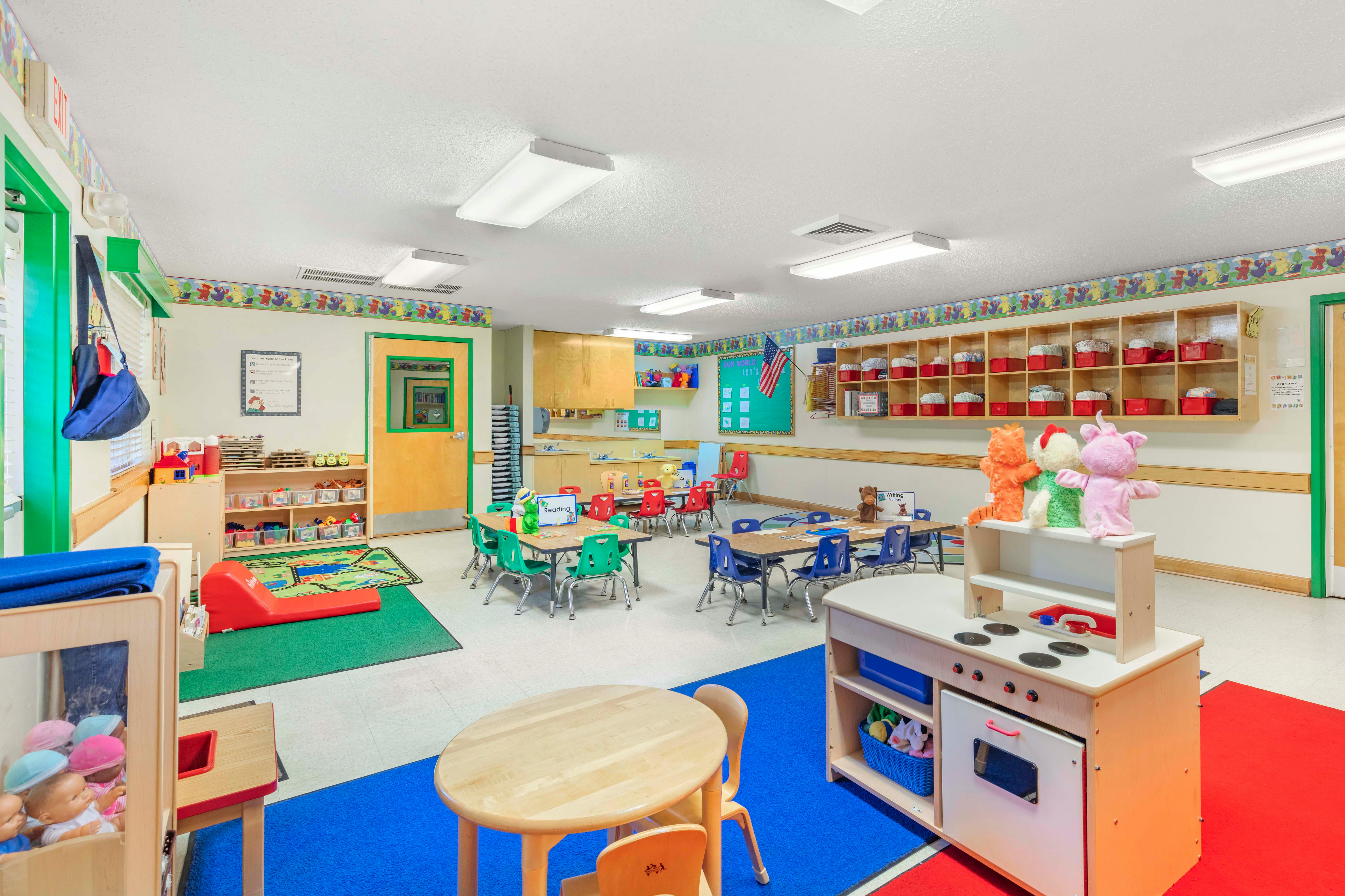 A colorful empty classroom with small tables, chairs, and play areas