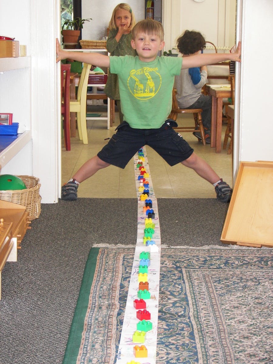 Child standing in a doorway with arms and legs spread wide over a line of blocks