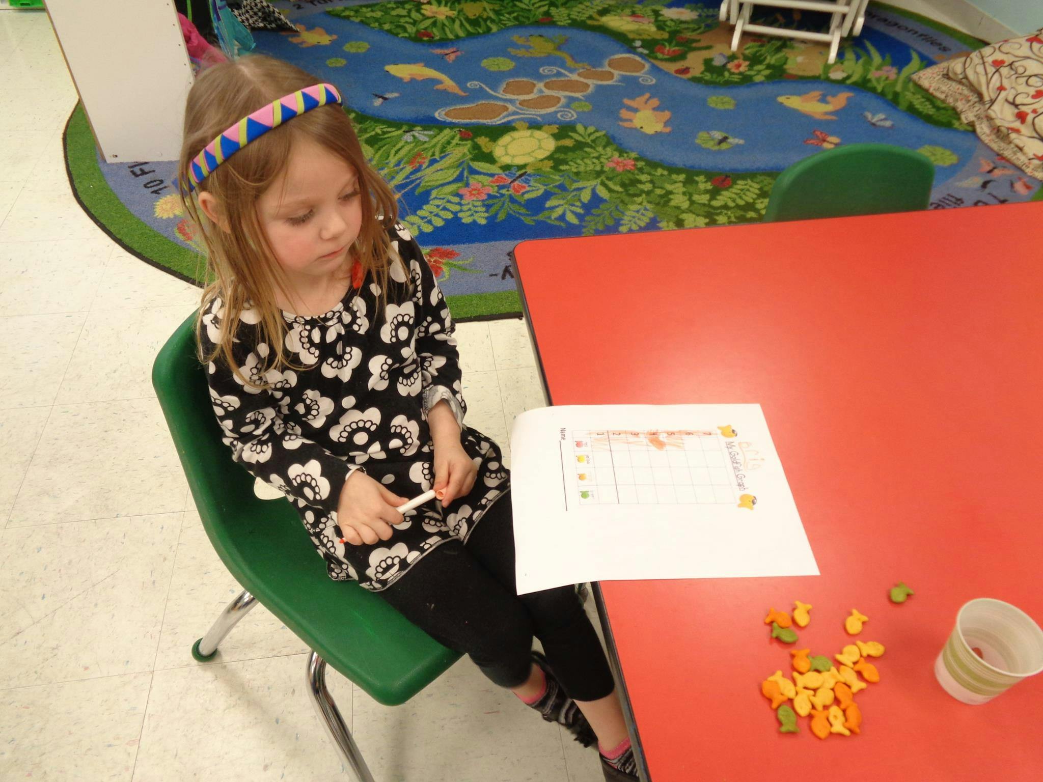 Child sitting at a red table with paper and small objects