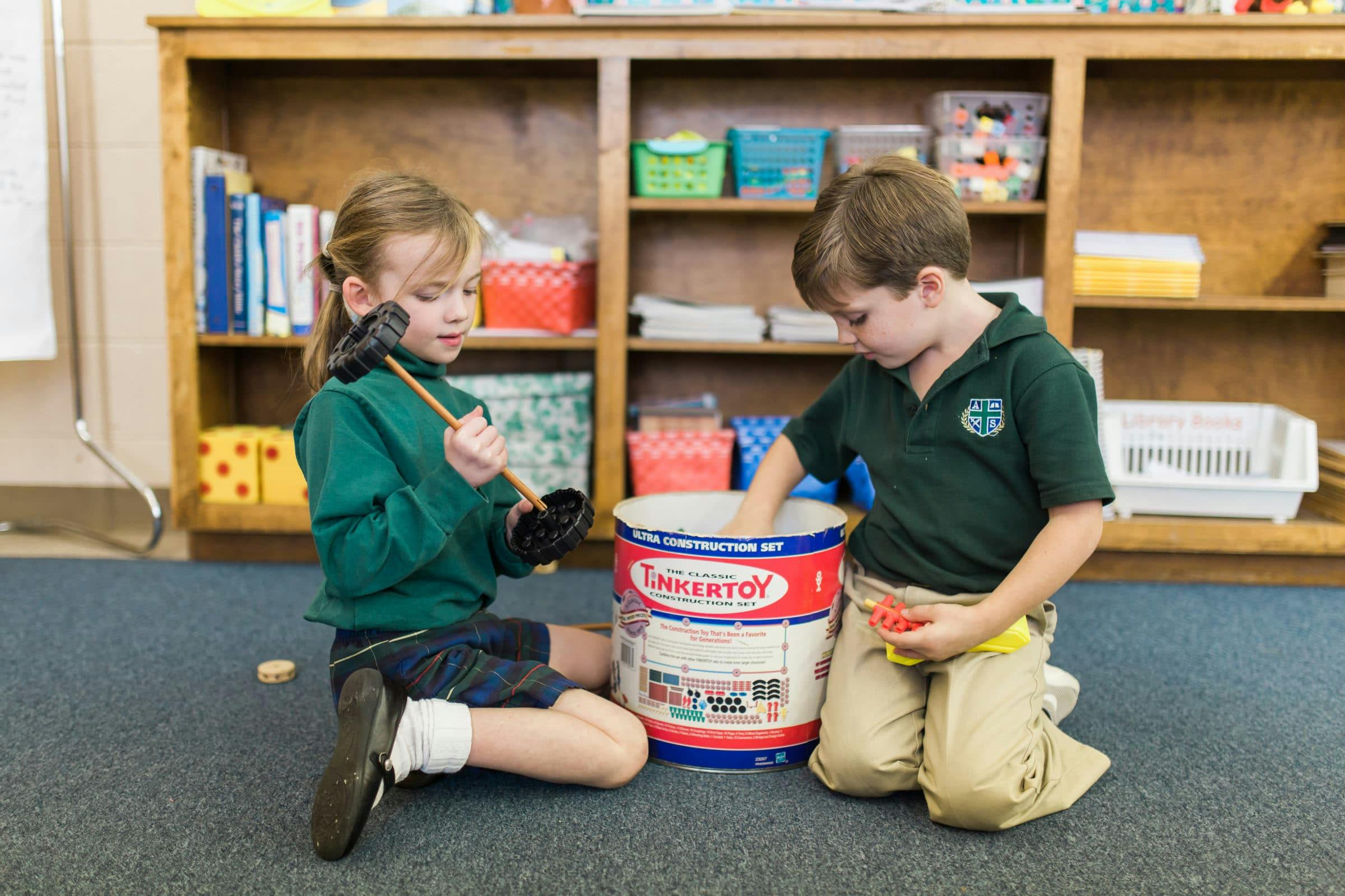 Two children playing with a Tinkertoy container on the floor