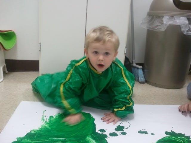 Child in green smock finger painting with green paint on paper