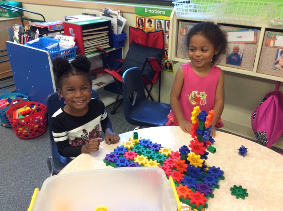 Two children playing with colorful interlocking gears at a table