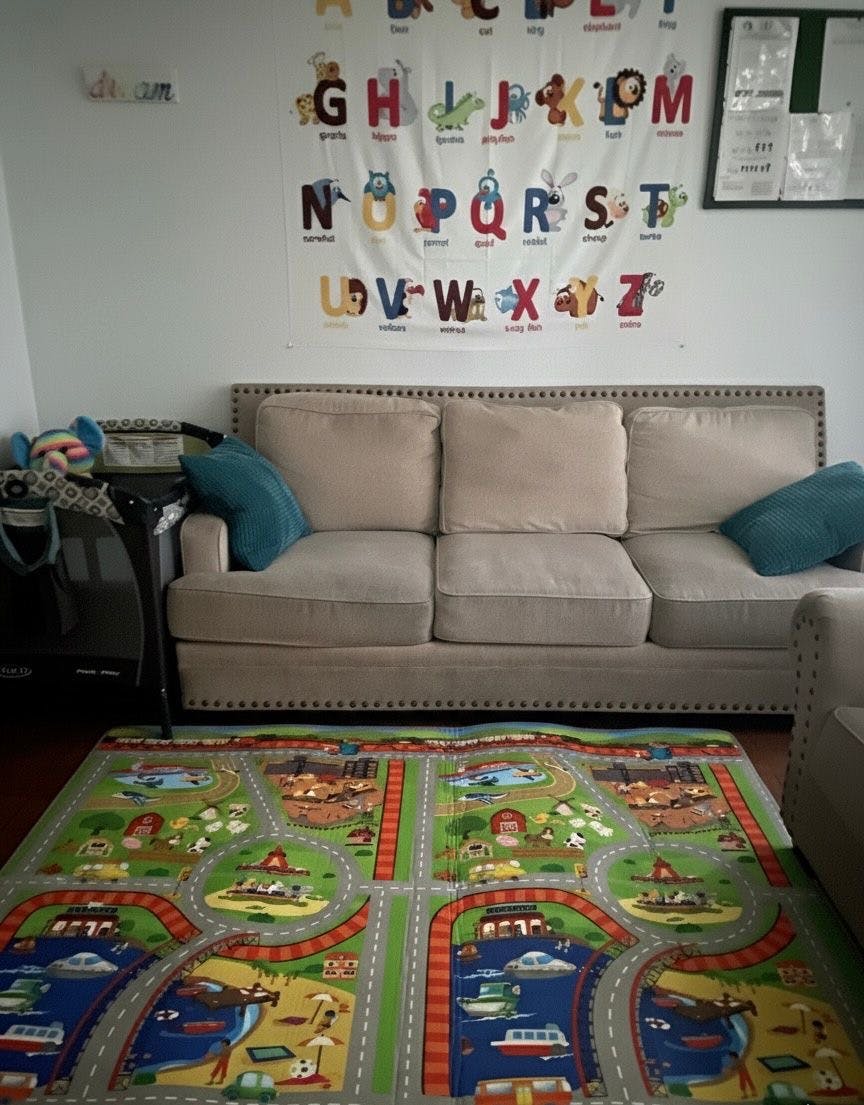 Living room with a sofa, alphabet chart on the wall, and a playmat on the floor