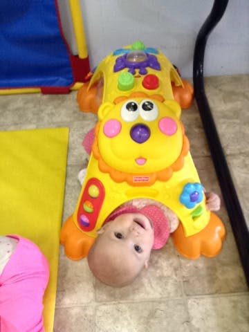 Child lying on back under a yellow lion-shaped toy