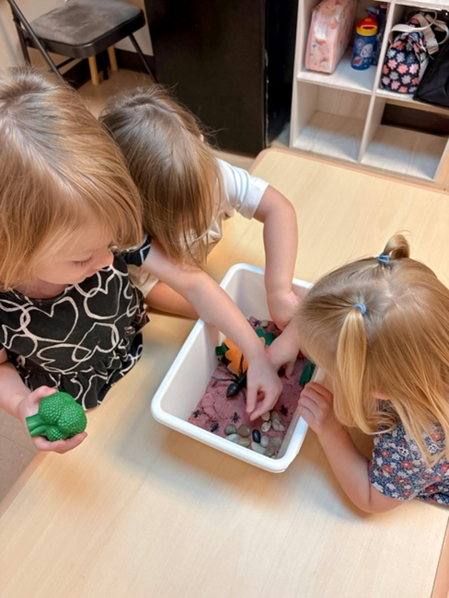 Three children playing with sensory bin toys on a table