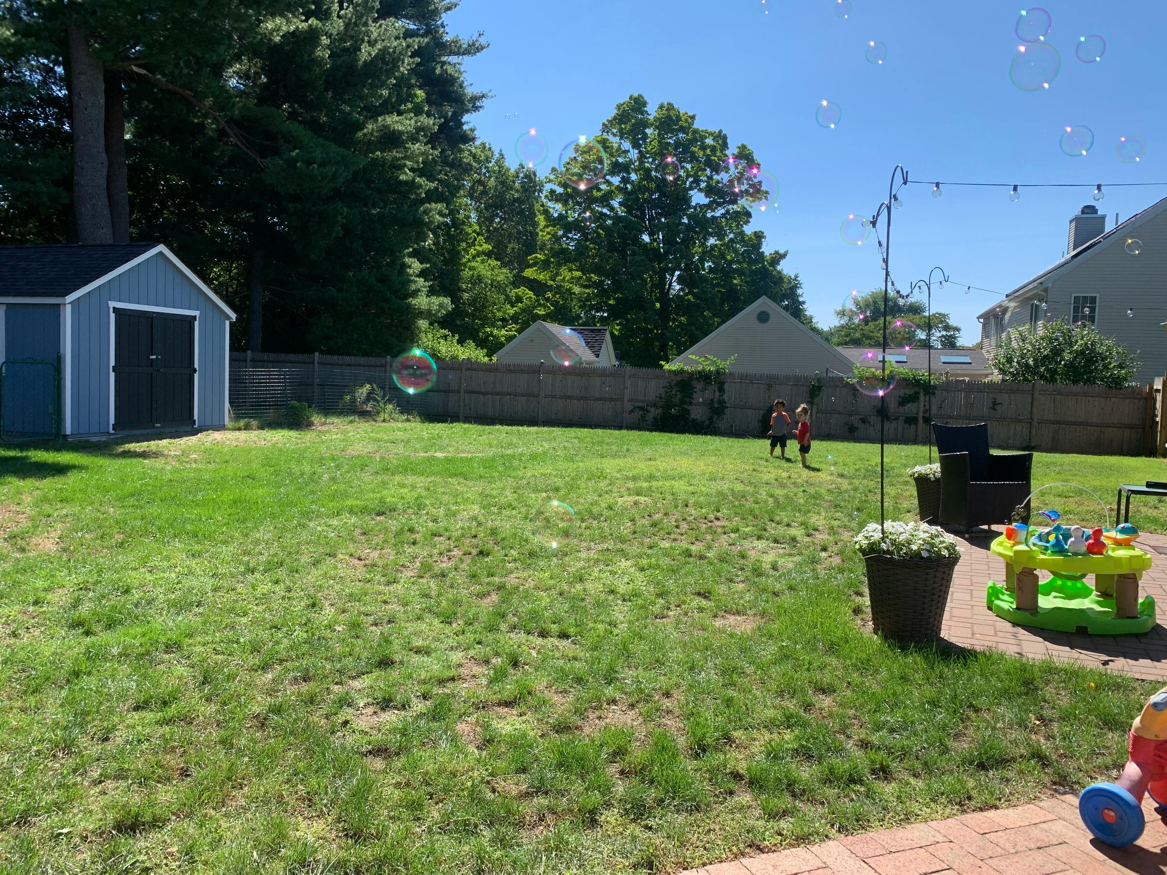 Two children running on a grassy lawn with bubbles floating in the air