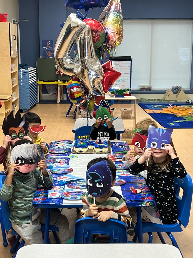 Children wearing character masks sitting at a table with balloons and cupcakes