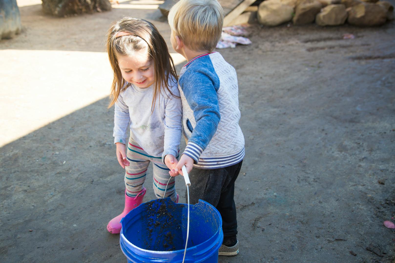 Two children holding a blue bucket together