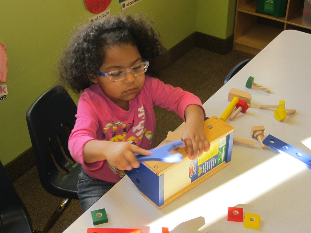 Child playing with a toy workbench and tools at a table