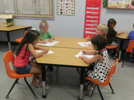 Children sitting at tables and drawing in a classroom