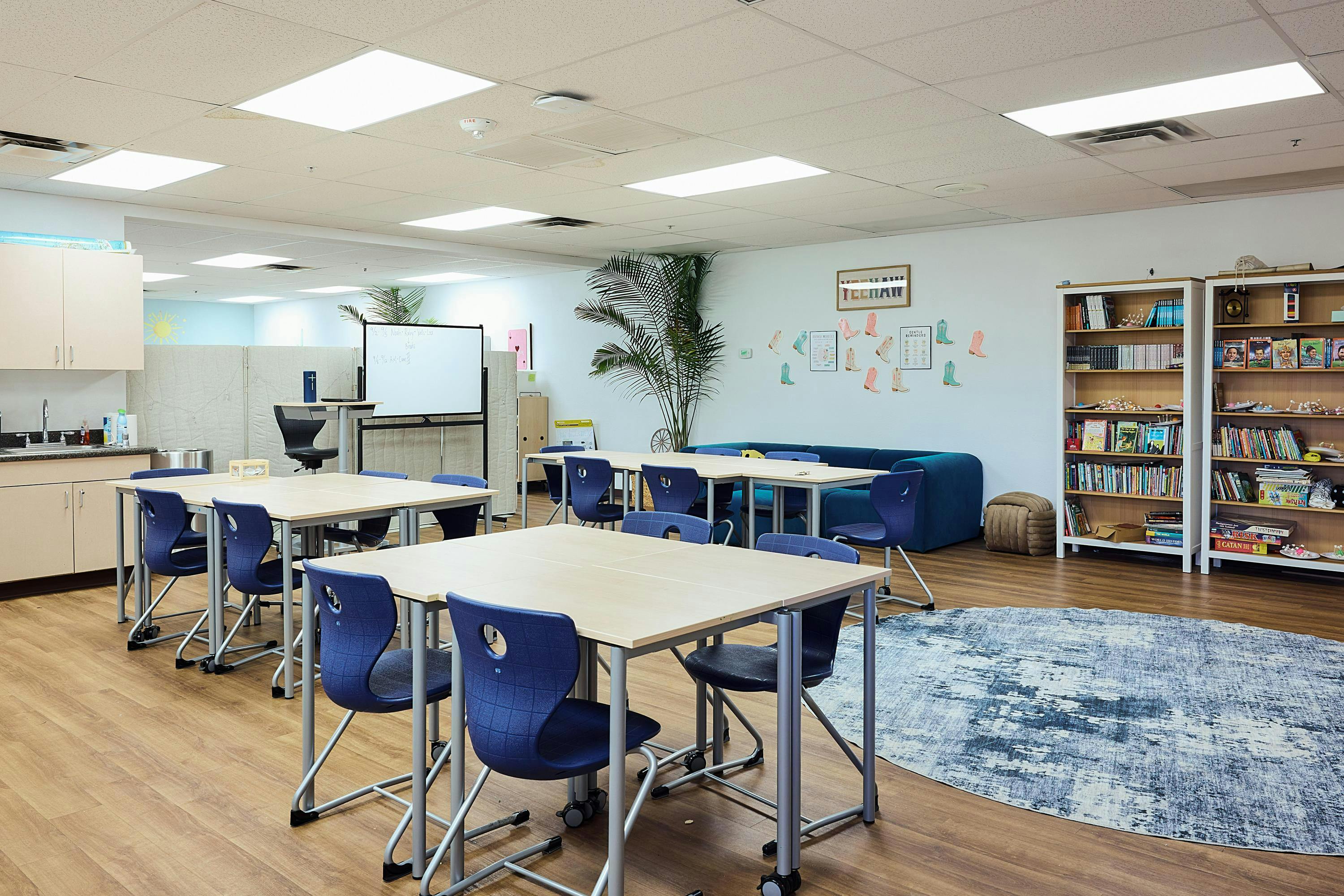 Classroom with light wood tables, blue chairs, whiteboards, and bookshelves