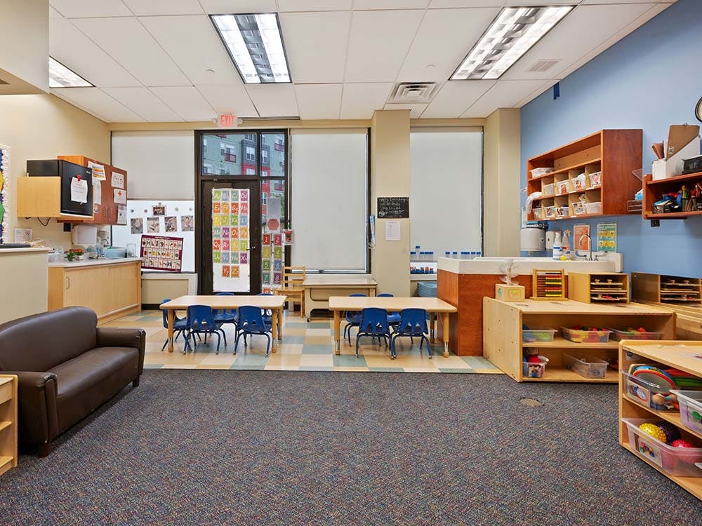 Classroom with small tables and chairs, sofa, and shelves with toys