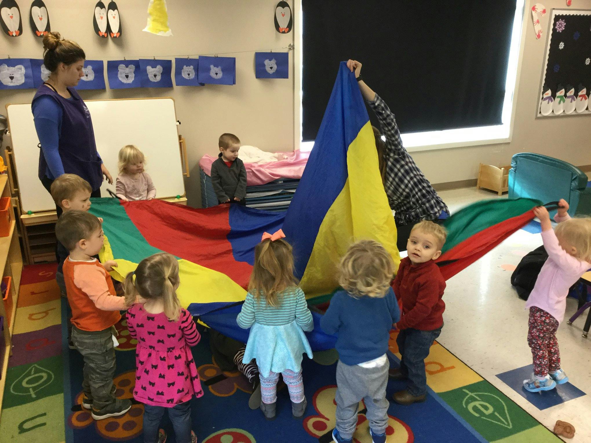 Adult and children playing with a colorful parachute in a classroom