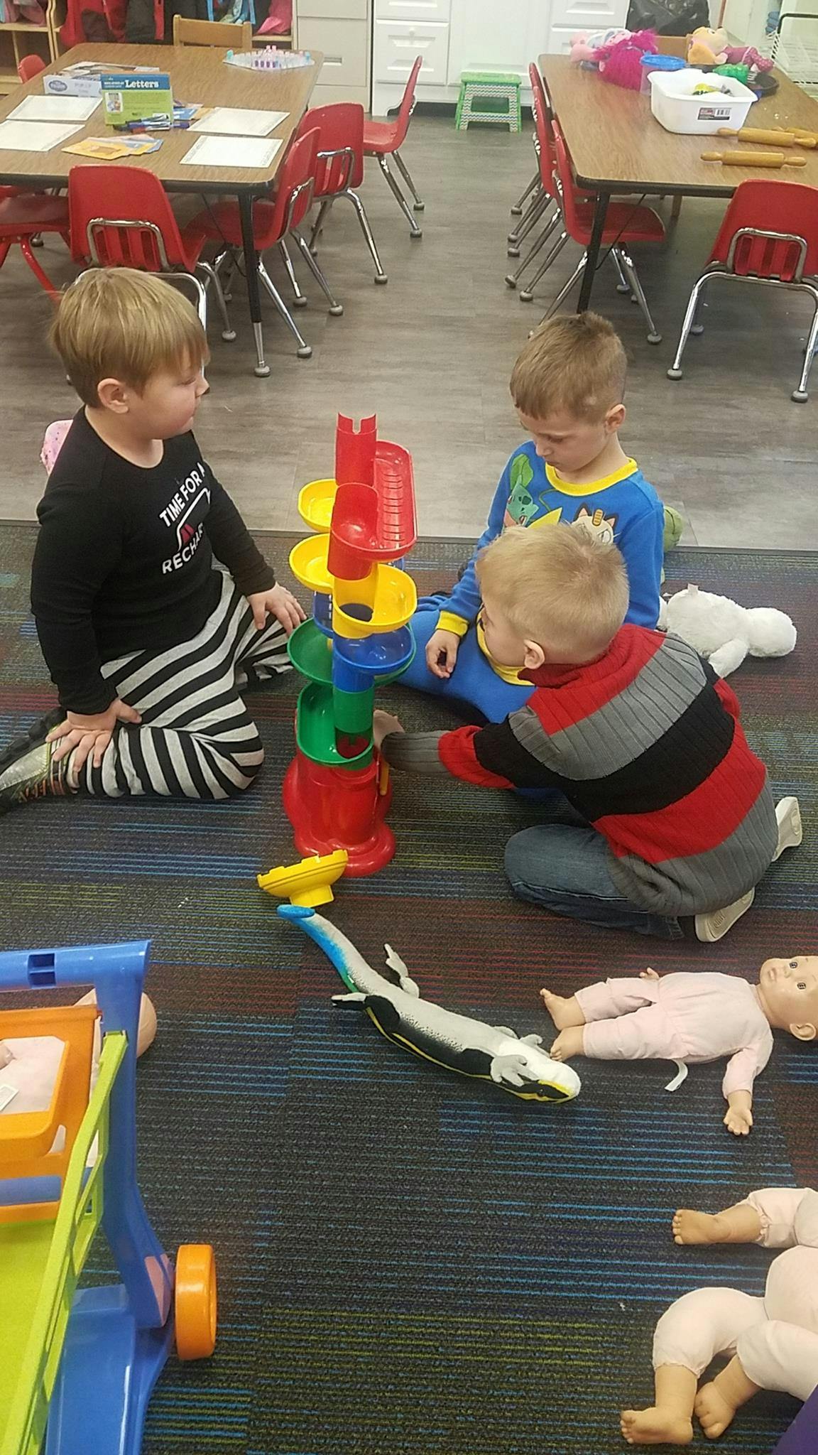 Three children playing with a colorful ball run toy on the floor