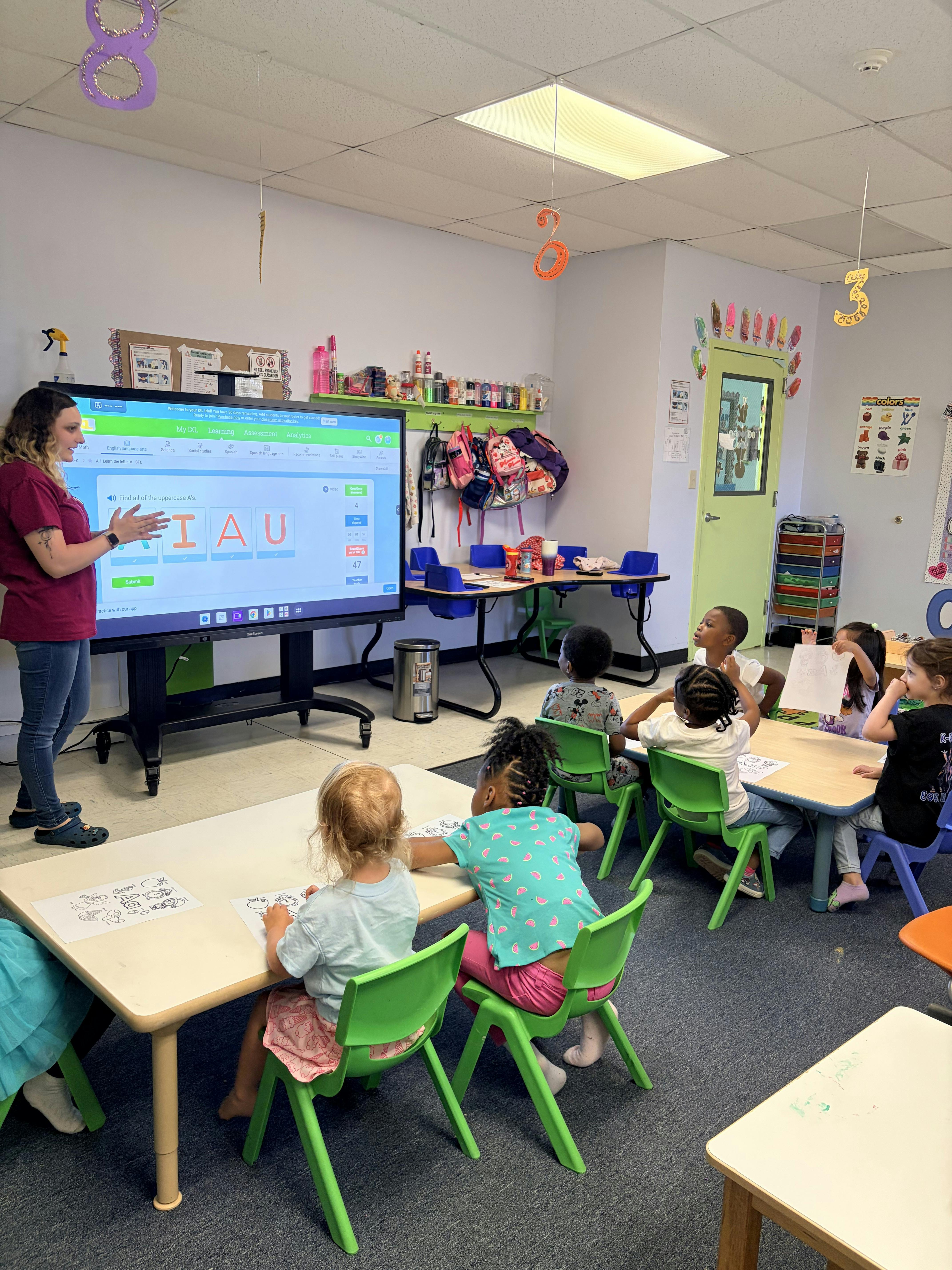 Teacher and children in a classroom looking at an interactive screen with letters