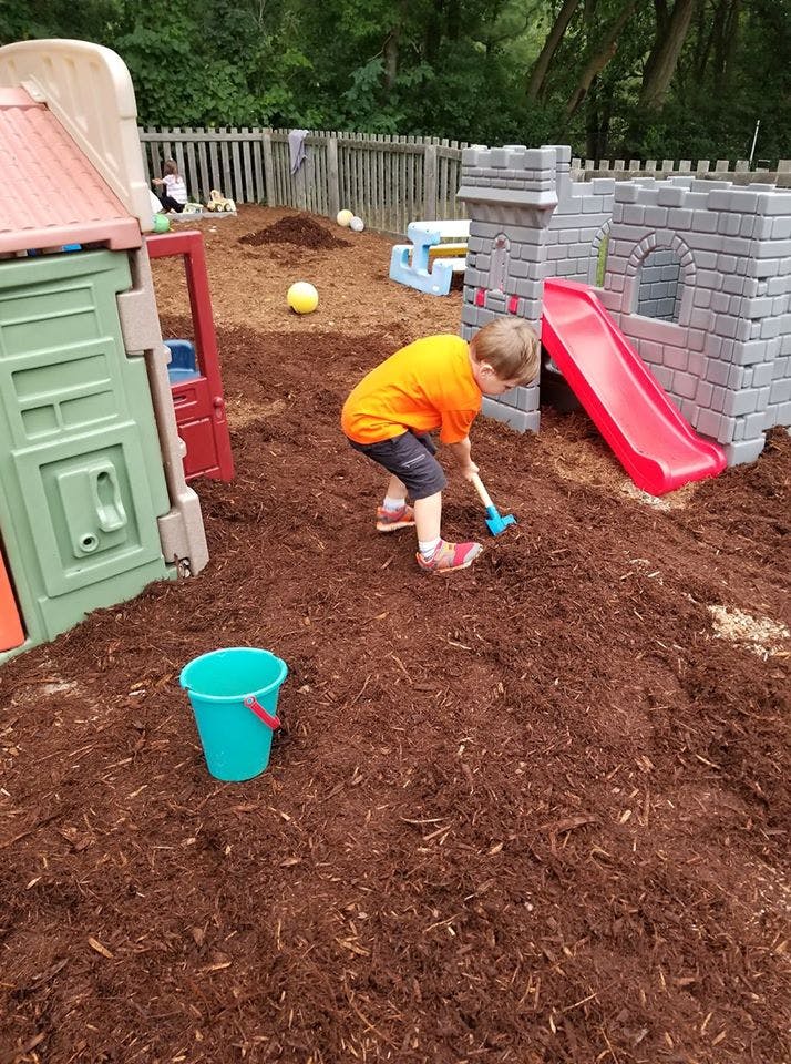Child playing with a shovel in wood chips next to a play structure