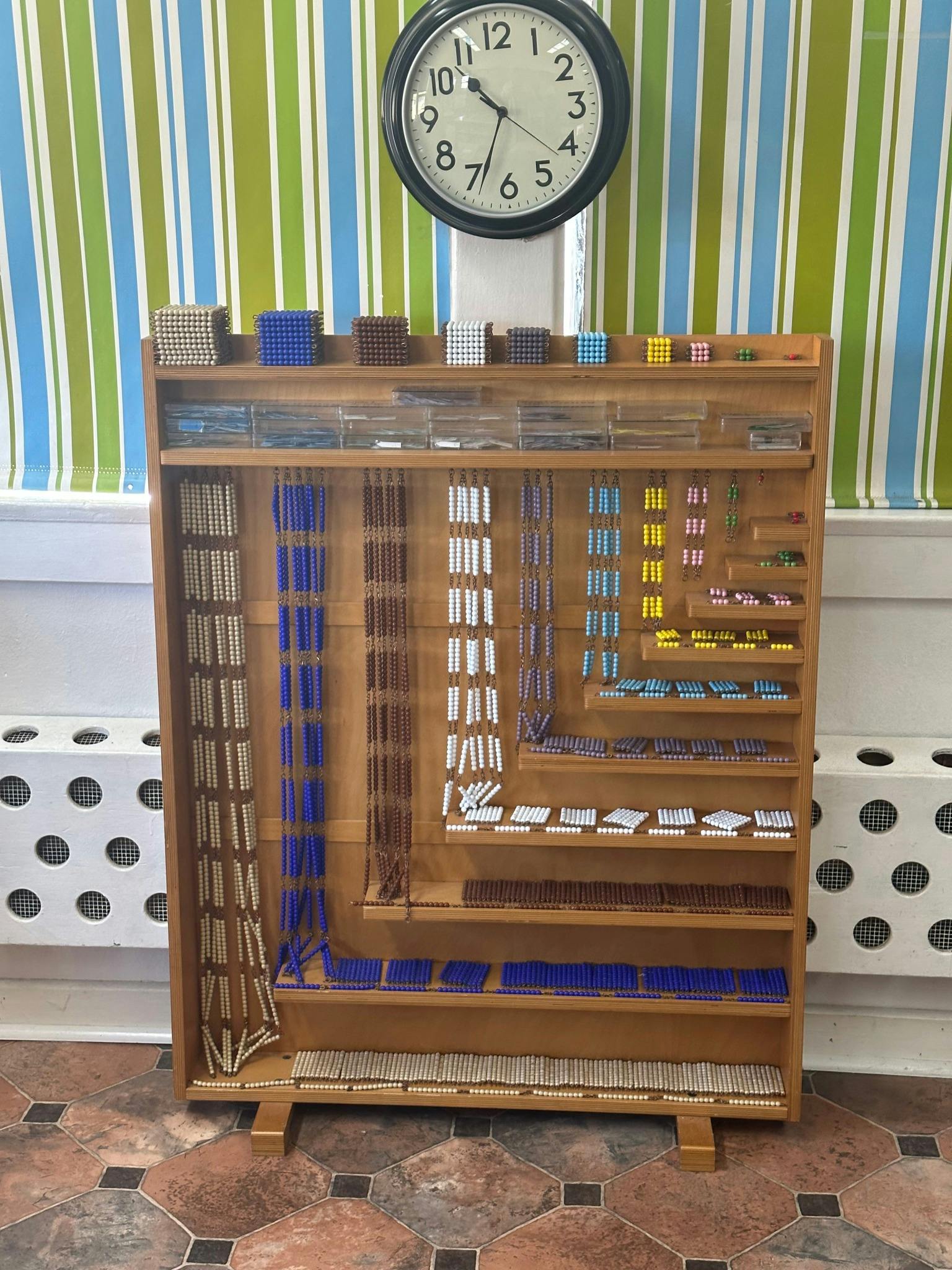 Wooden shelf with various colored beads and blocks, a clock above