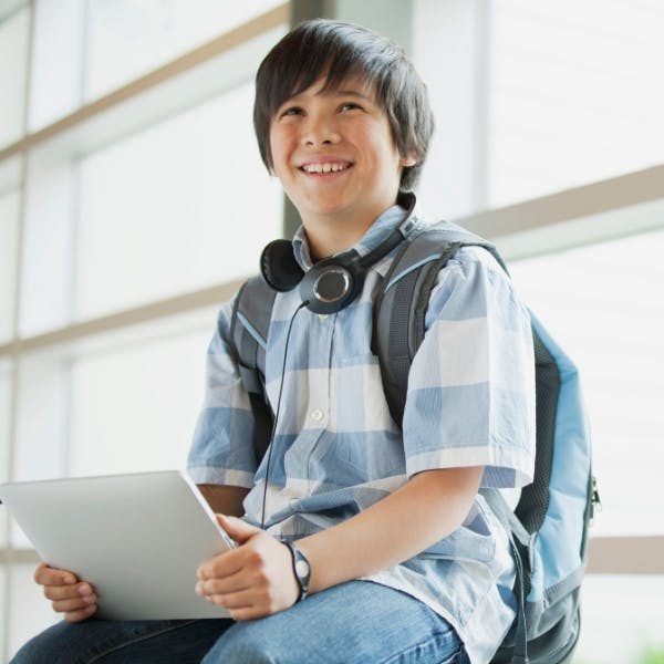 Child with headphones around neck holding a tablet