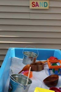Sand play table with buckets and toys, sign above reads SAND