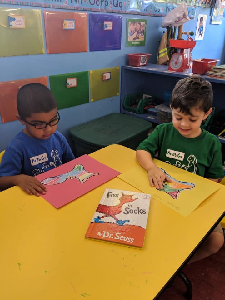 Two children coloring at a yellow table in a classroom
