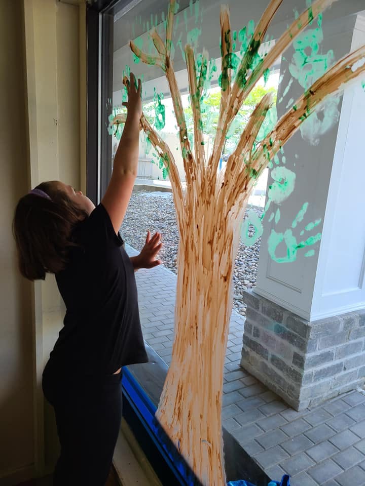 Child painting a tree on a window