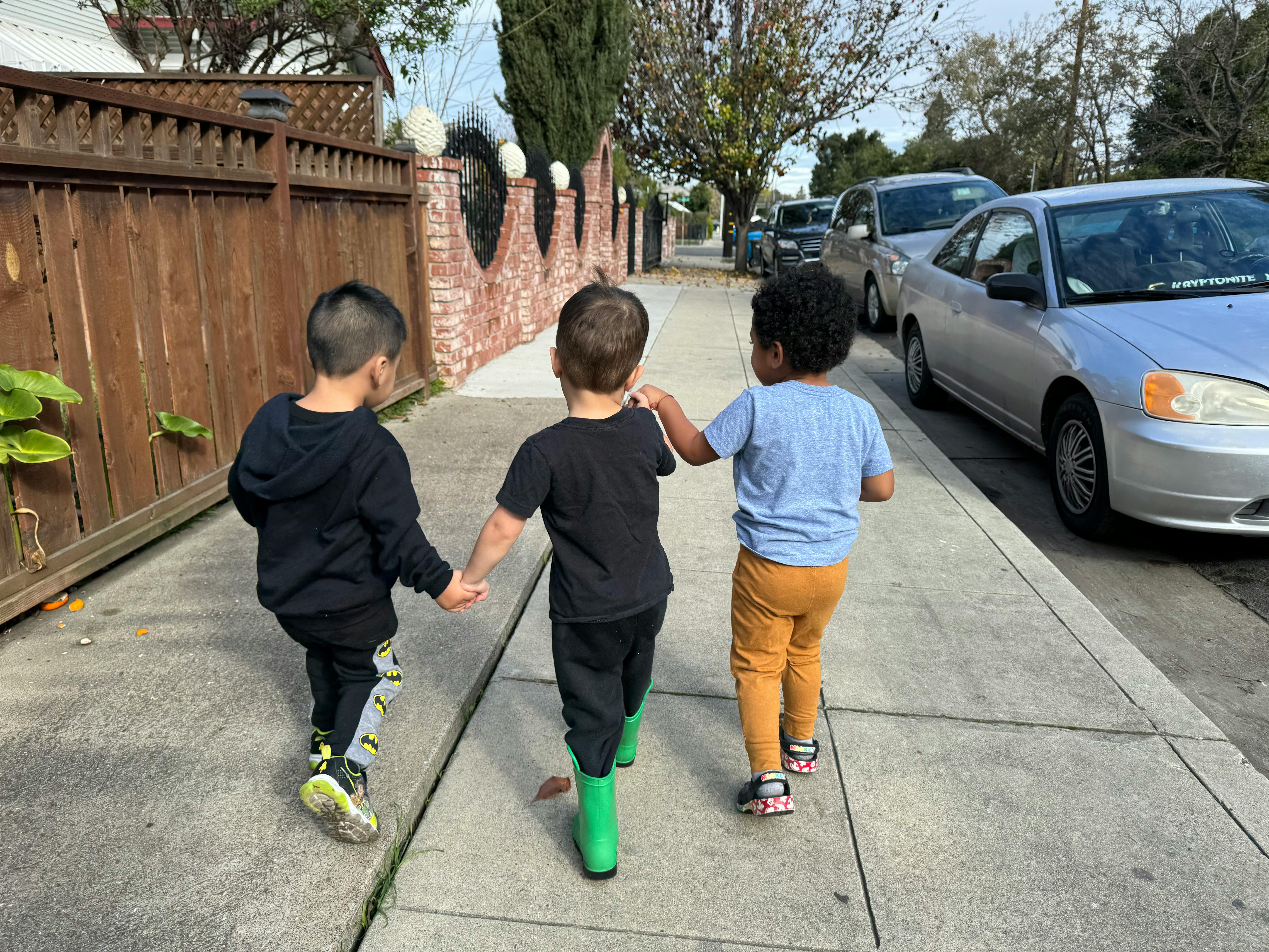 Three children walking on a sidewalk, holding hands