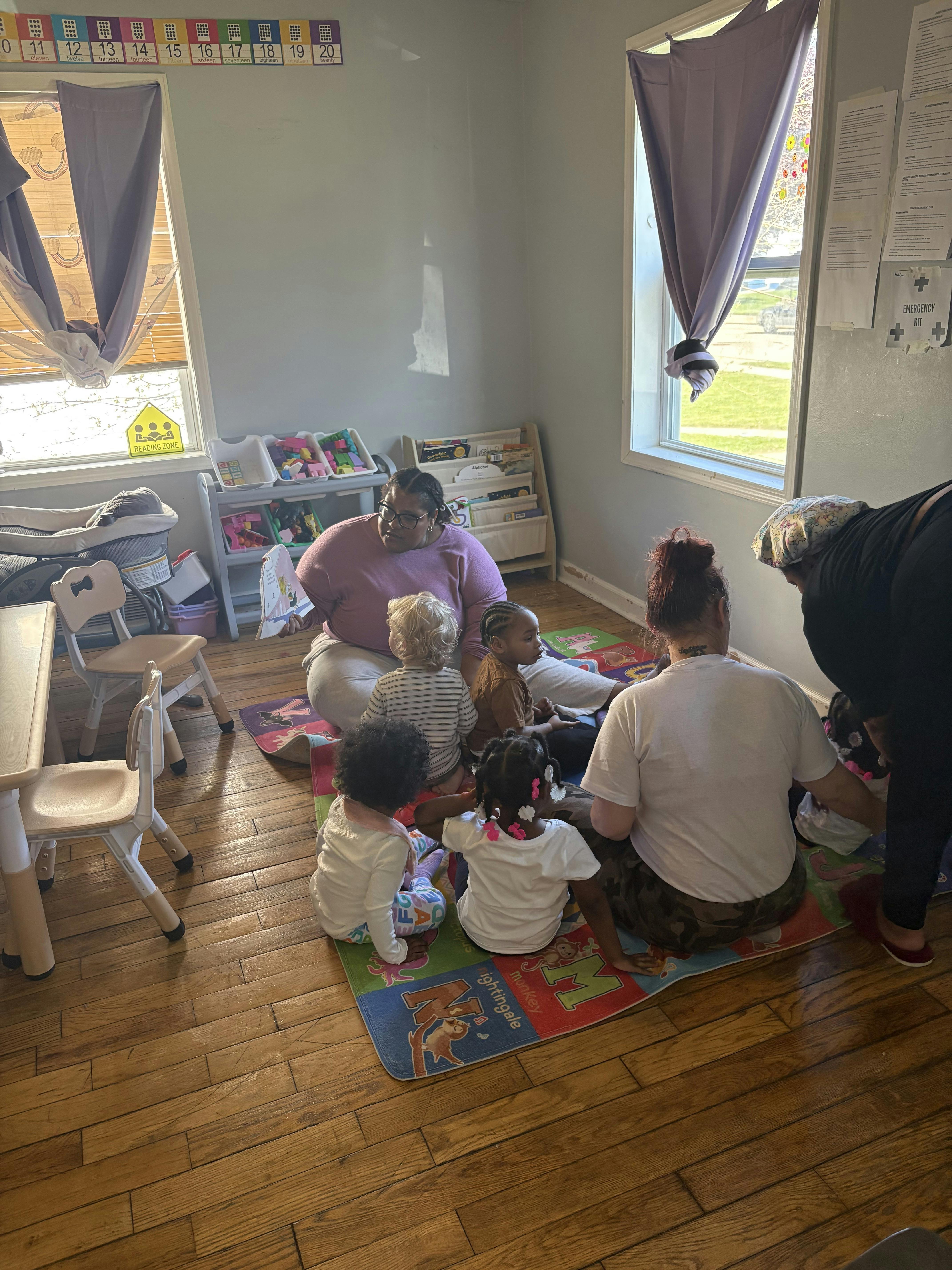 Adult reading a book to a group of children sitting on a mat in a classroom