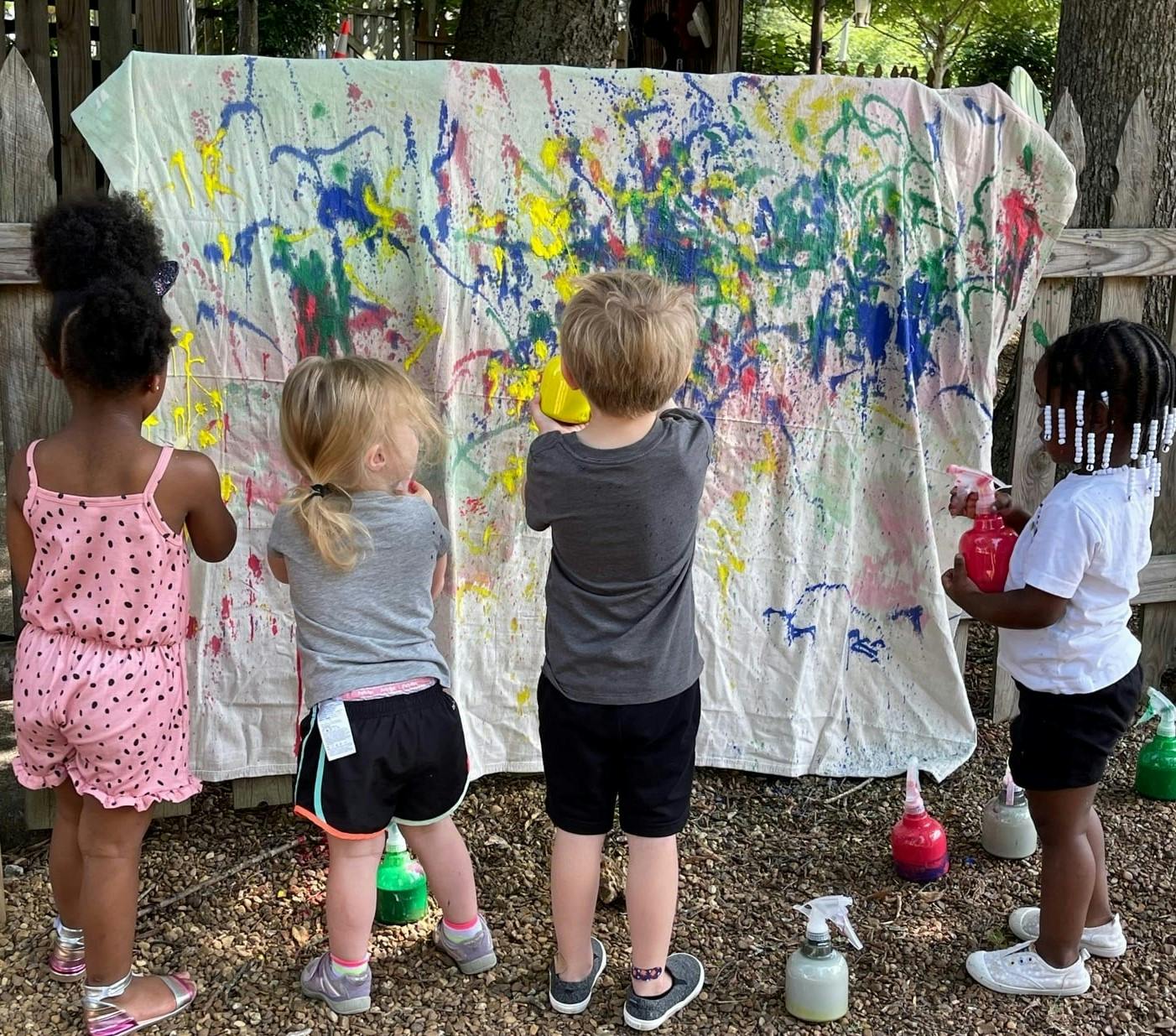 Children painting on a large white sheet outdoors