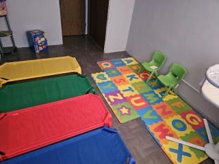 Four colorful cots and two alphabet rugs in a room