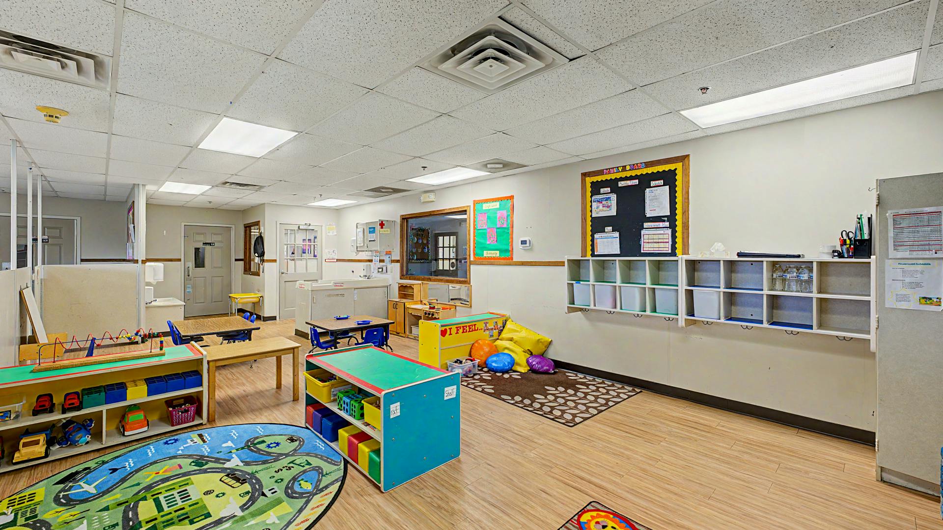 Playroom with small tables, chairs, toy shelves, and a road-themed rug