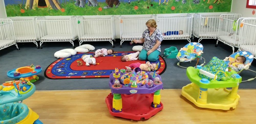 Person kneeling on a rug with multiple babies and baby play items