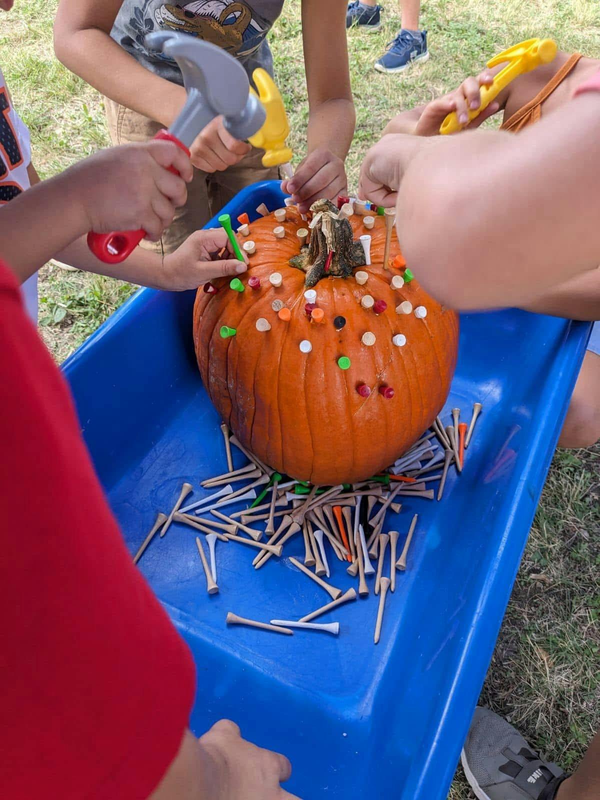 Children using hammers to drive golf tees into a pumpkin