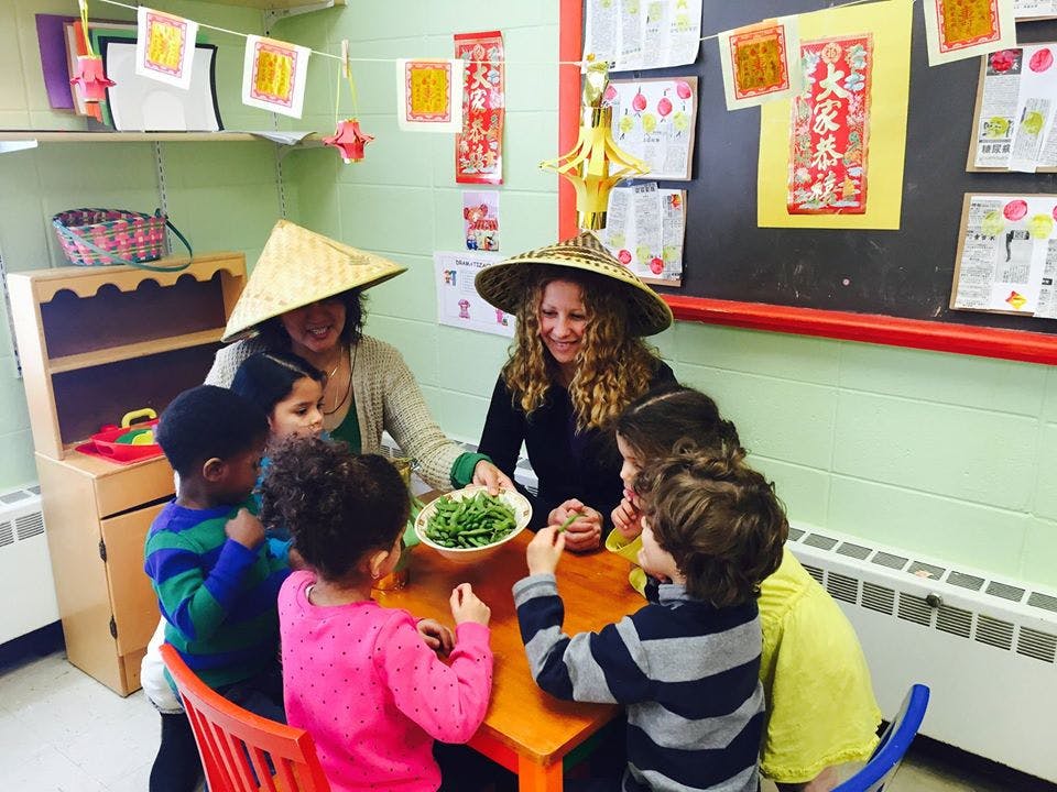 Two people in hats with children around a table with a bowl of greens