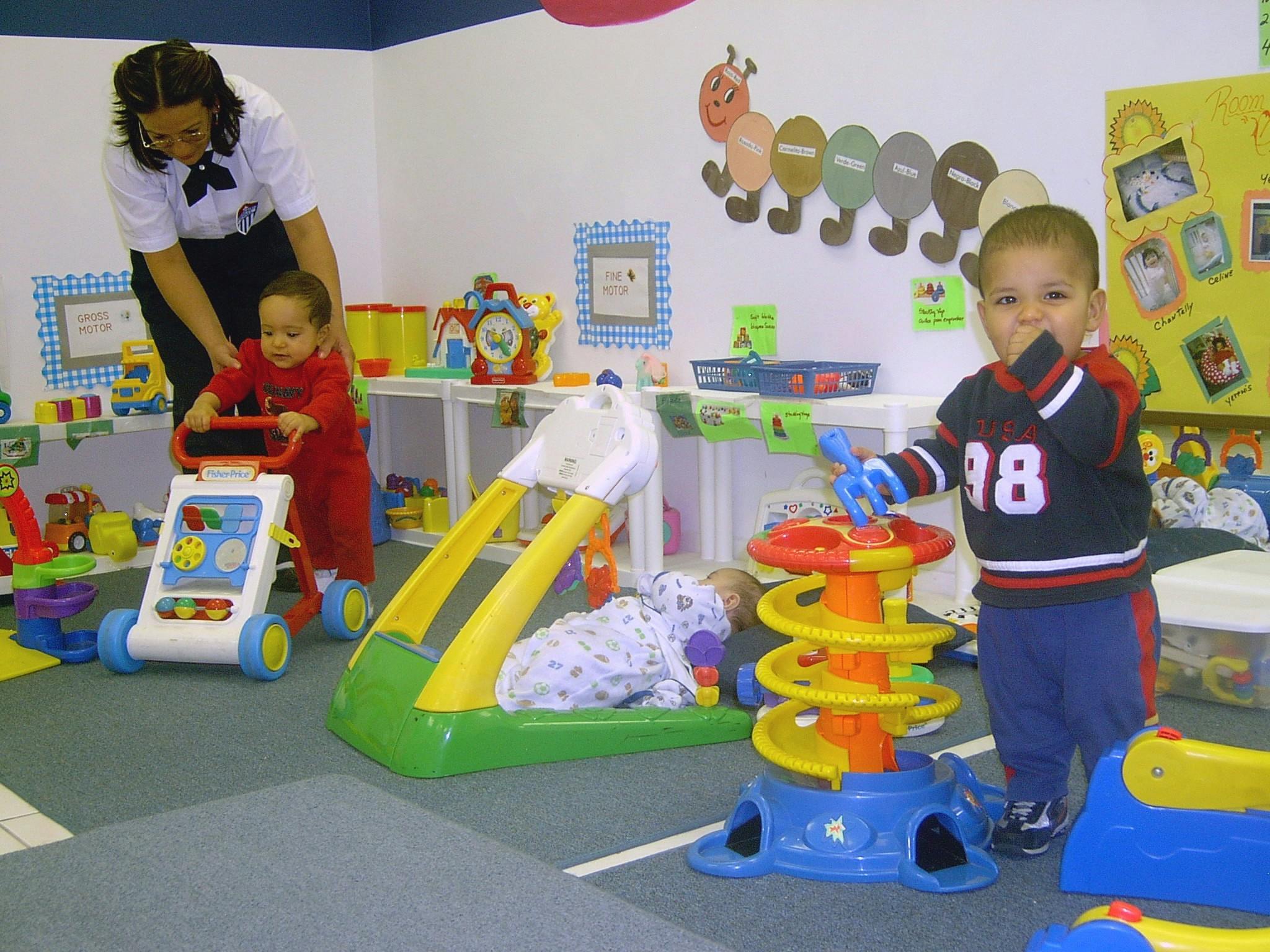 Adult helping a child with a walker, another child playing with a toy