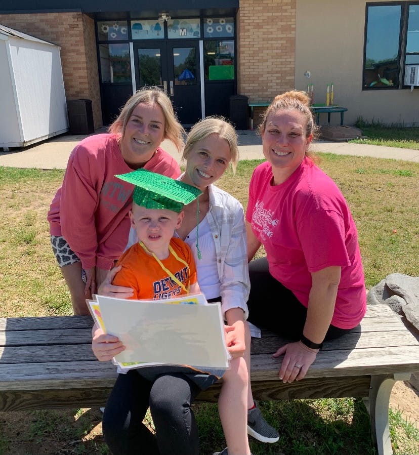 Three people and a child in a graduation cap holding papers