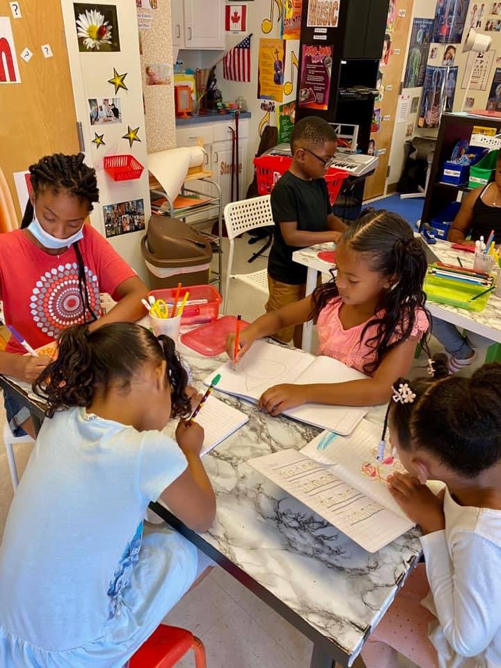 Children writing and drawing at a table in a classroom