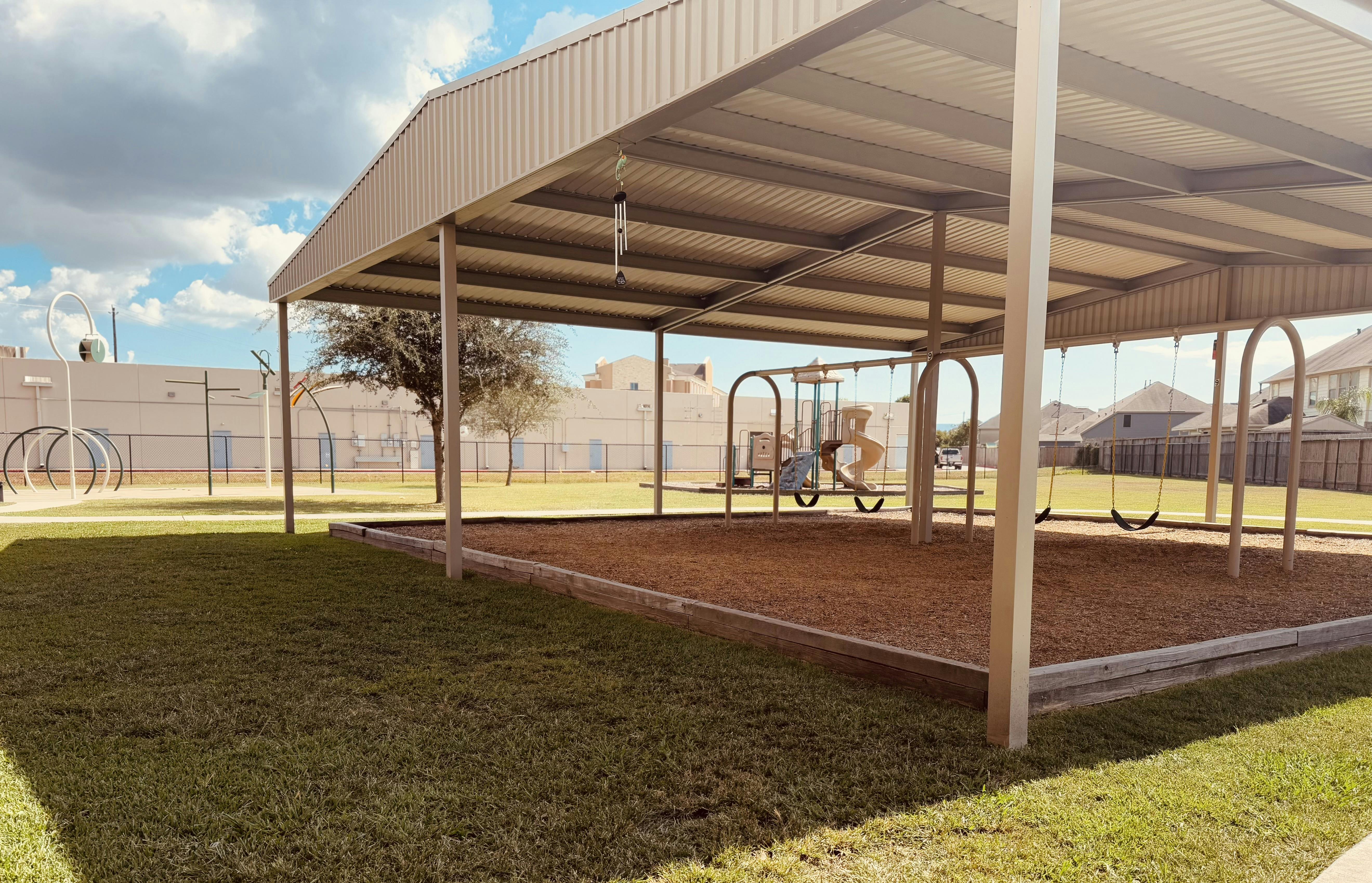 Covered outdoor playground with swings and play structures on wood chips