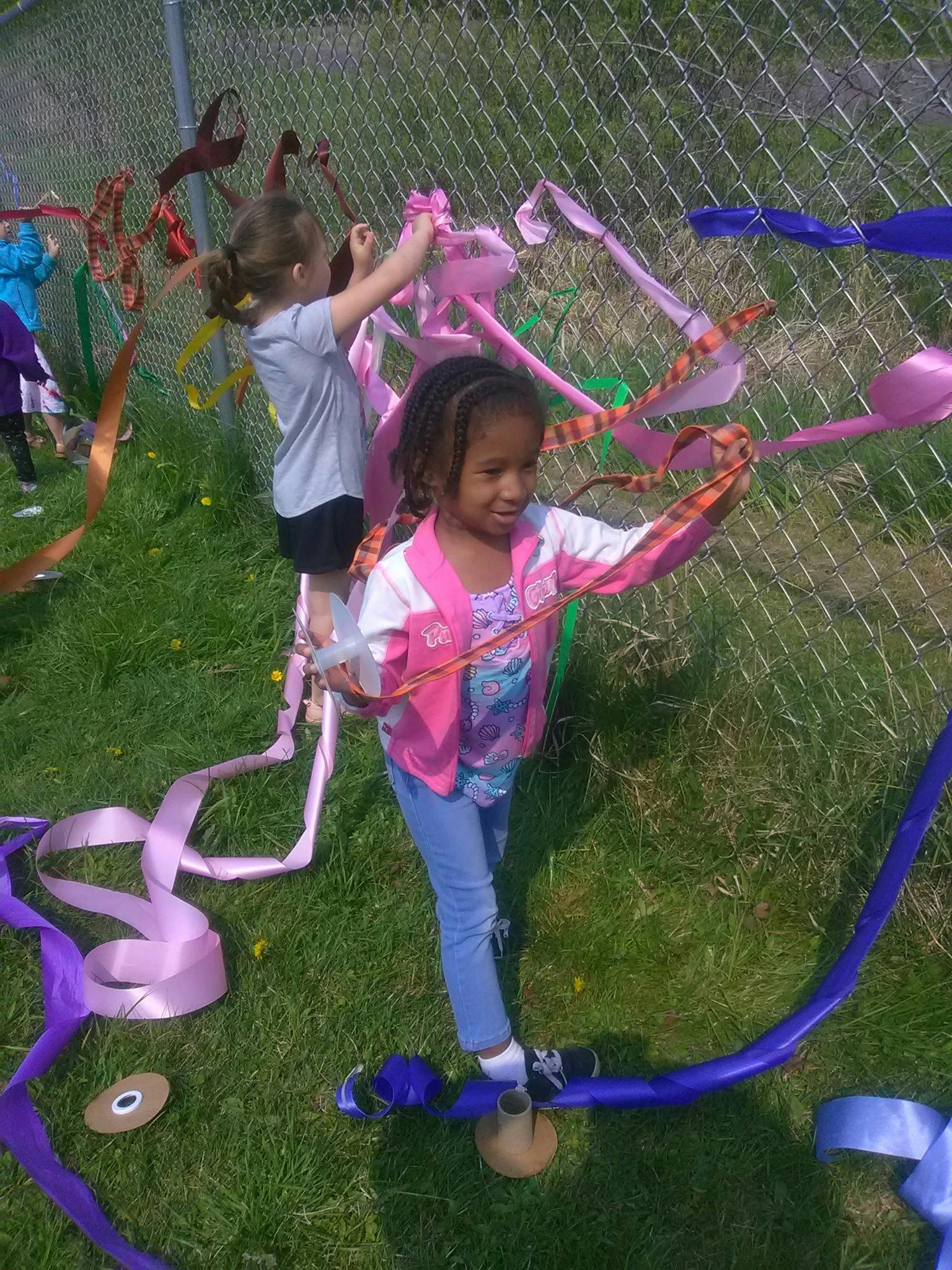 Two children tying colorful ribbons to a chain-link fence