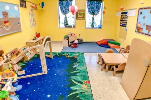 Empty classroom with colorful rugs, small tables, and toys
